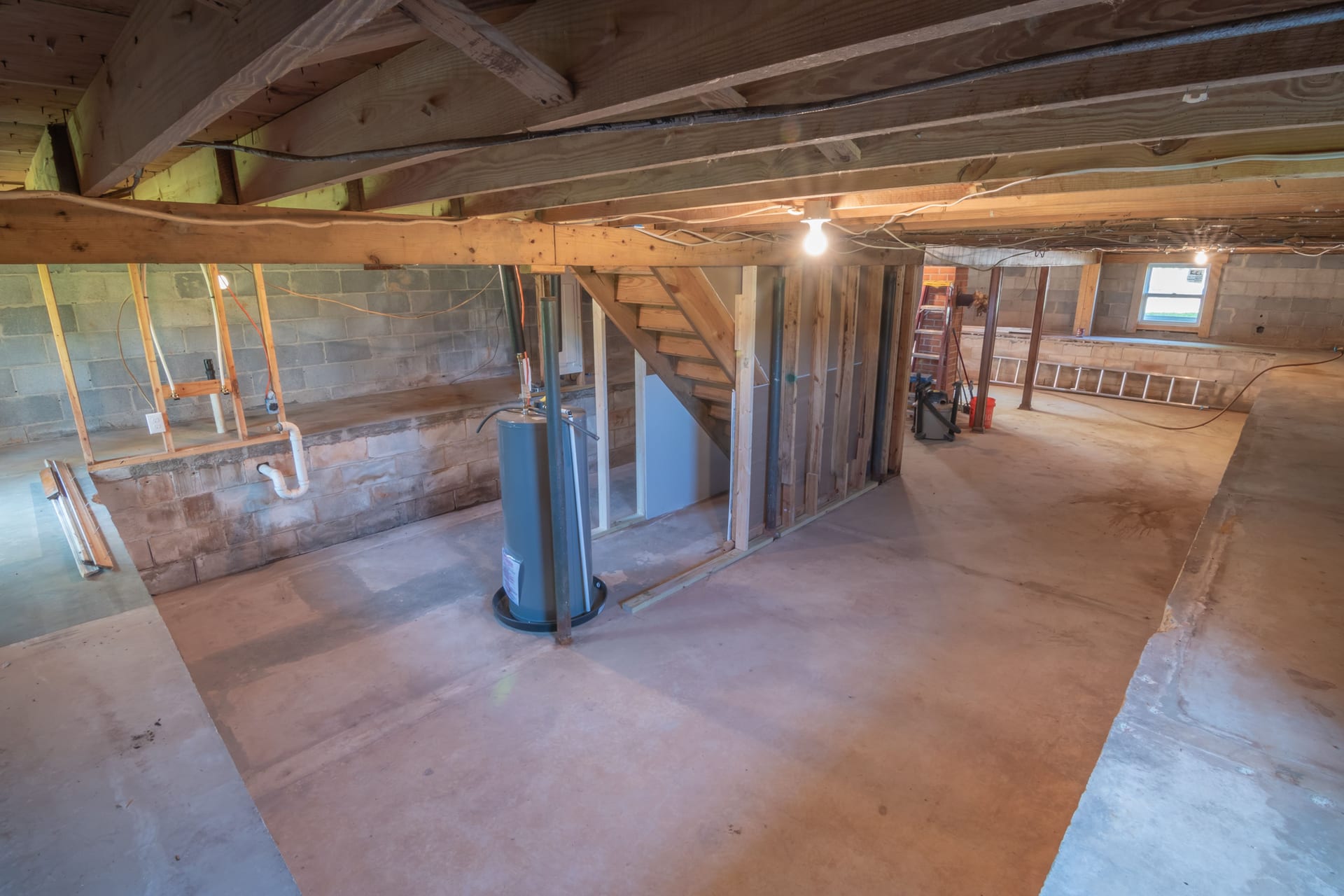 Unfinished basement with exposed wooden joists, concrete walls, and utility piping
